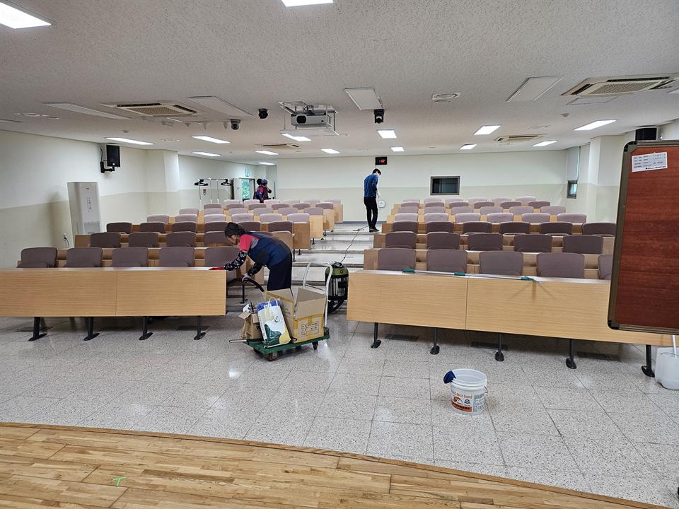 강당 바닥과 좌석을 정리하는 미화 작업